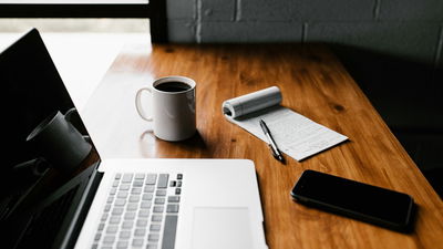 A photograph showing a laptop and a notepad on top of a table.
