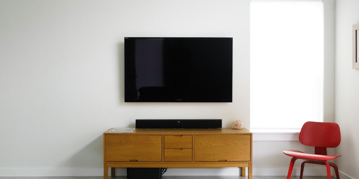 Large screen TV on white wall with a brown TV stand and red chair