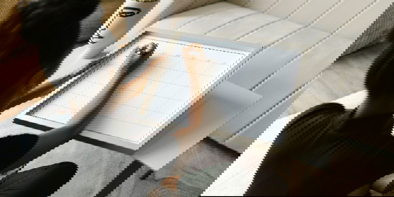 Woman sitting in the floor writing on a wall calendar.