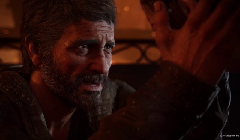 An image from The Last of Us Part 1 game remake, with a man emoting with pain on his face, holding a girl's face in his hands, trying to comfort her. 
