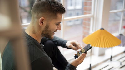 man happily looking at phone in had near window