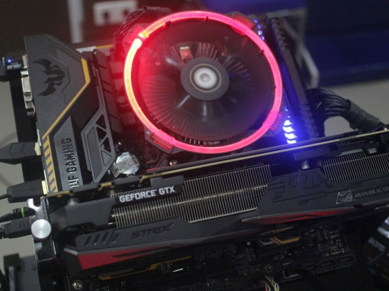 An open test bench PC showing a graphics card and CPU cooler in red lighting
