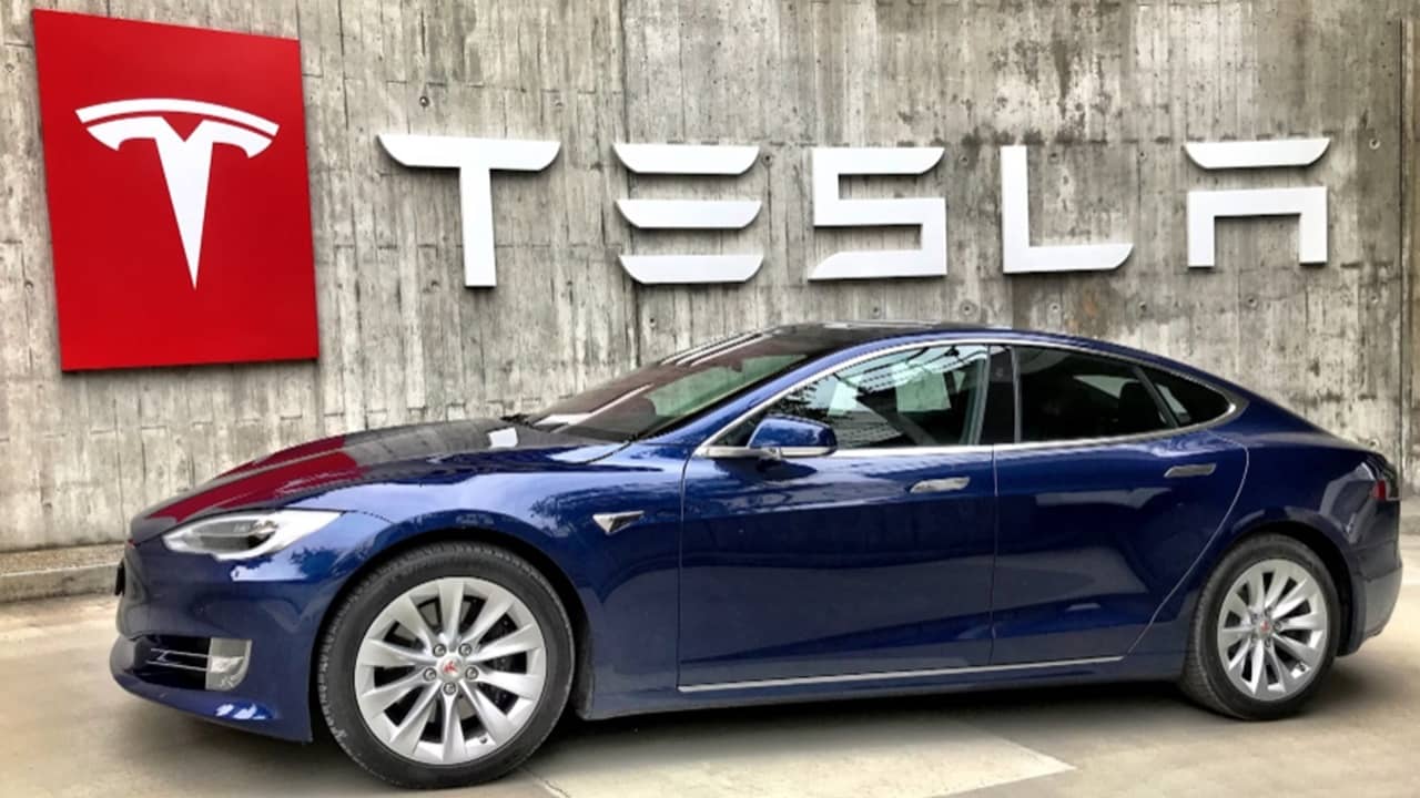 Tesla in front of Tesla sign.